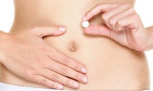 Birth control pill, Contraceptive pills, Vitamin pill, pills for better digestion or pills against menstrual pain. Woman holding white tablet in front of stomach. Close up.